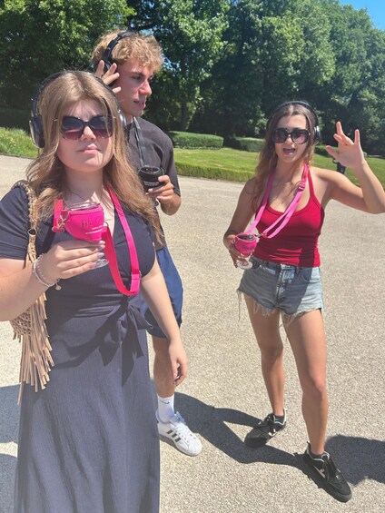 Three people outdoors, one holding a pink bag and another making a peace sign. 4