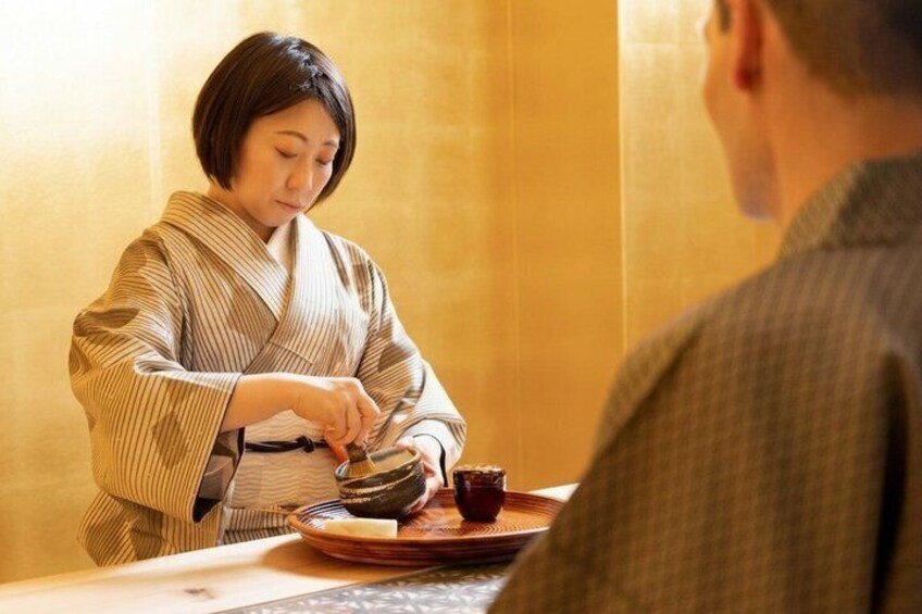 A person in traditional attire serving tea to another individual at a table. 1