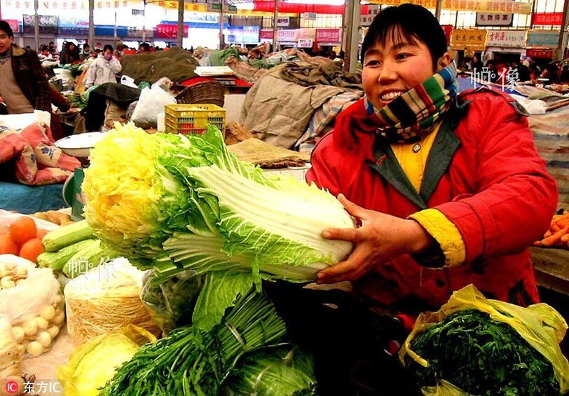 A person holding a large head of bok choy at a market with various vegetables and produce. 1