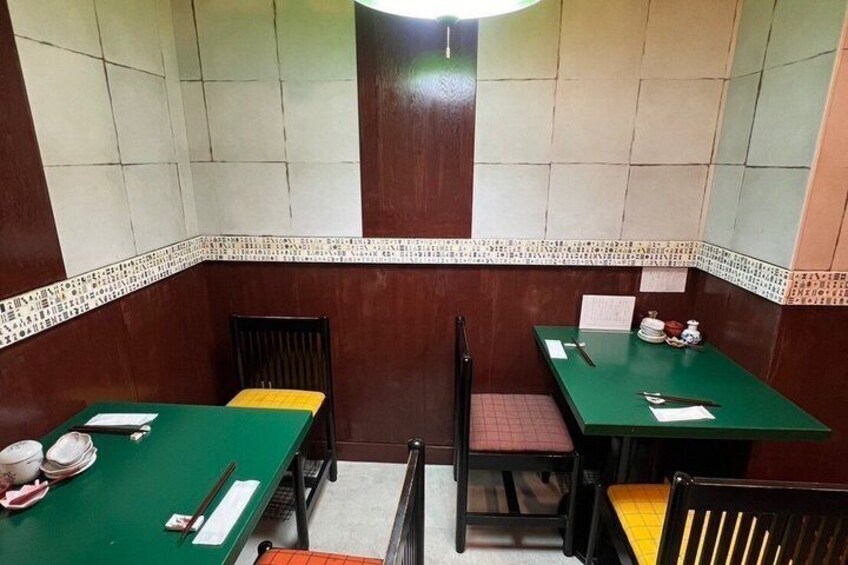 A restaurant interior with green tables and chairs, tiled walls, and a patterned border. 5