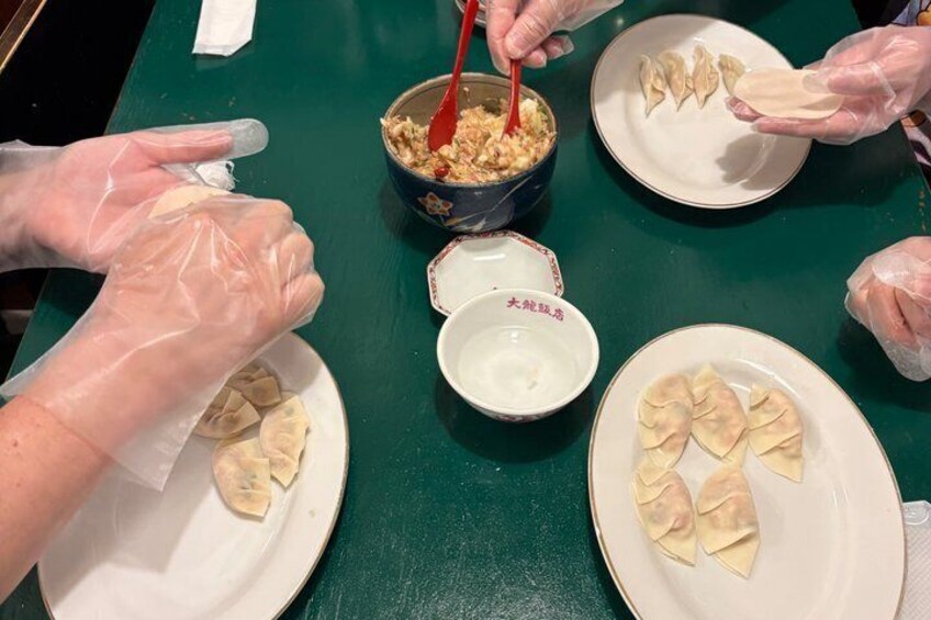 People preparing dumplings with a bowl of filling and a plate of dumplings. 4