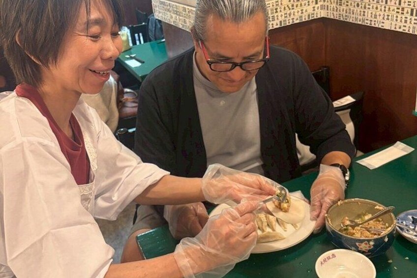 Two people preparing food, one wearing gloves, at a table with a bowl of ingredients and a plate. 4