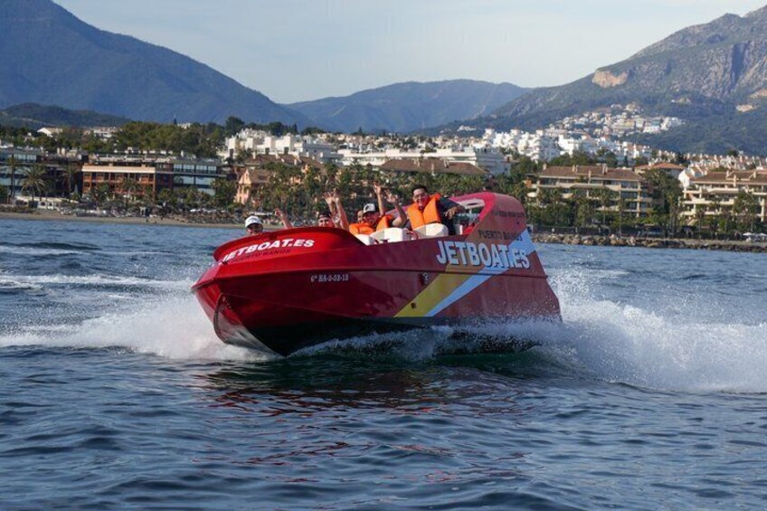 A red speedboat with 'JETBOATS' branding on a lake with a mountainous backdrop. 1