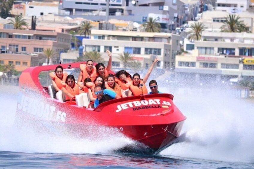 A red jetboat with 'JETBOAT MARBELLA' written on it, moving through water with passengers. 5