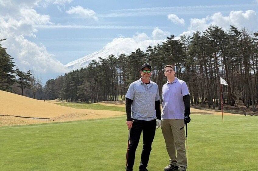 Two people standing on a golf course with a mountain in the background. 4