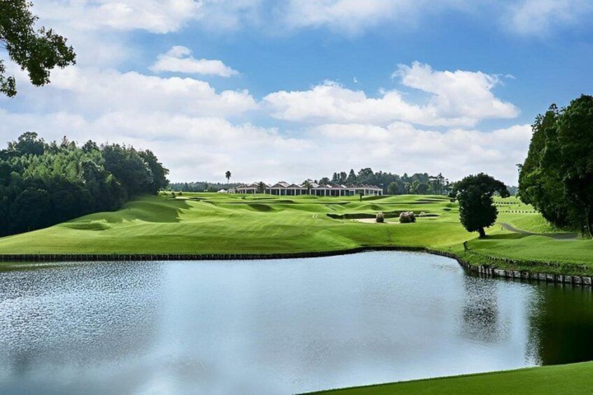 A golf course with a pond, green hills, and a clubhouse in the distance. 3