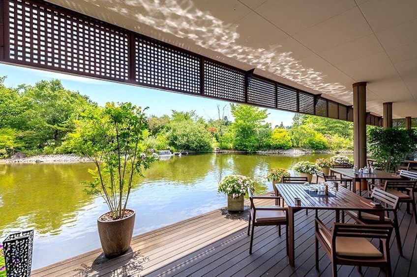 A wooden deck overlooking a calm river, surrounded by lush greenery and potted plants. 2