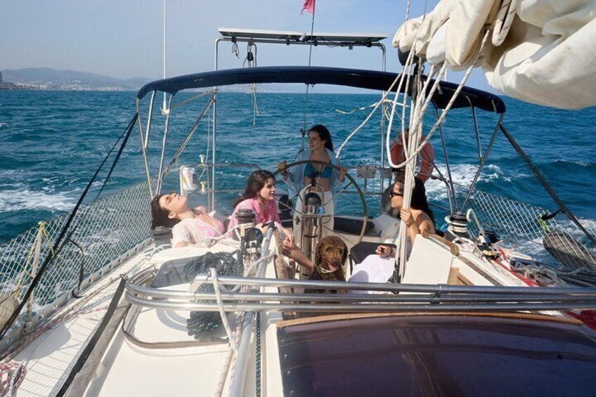 A sailboat with people on deck, a woman steering, and a dog on the bow. 5