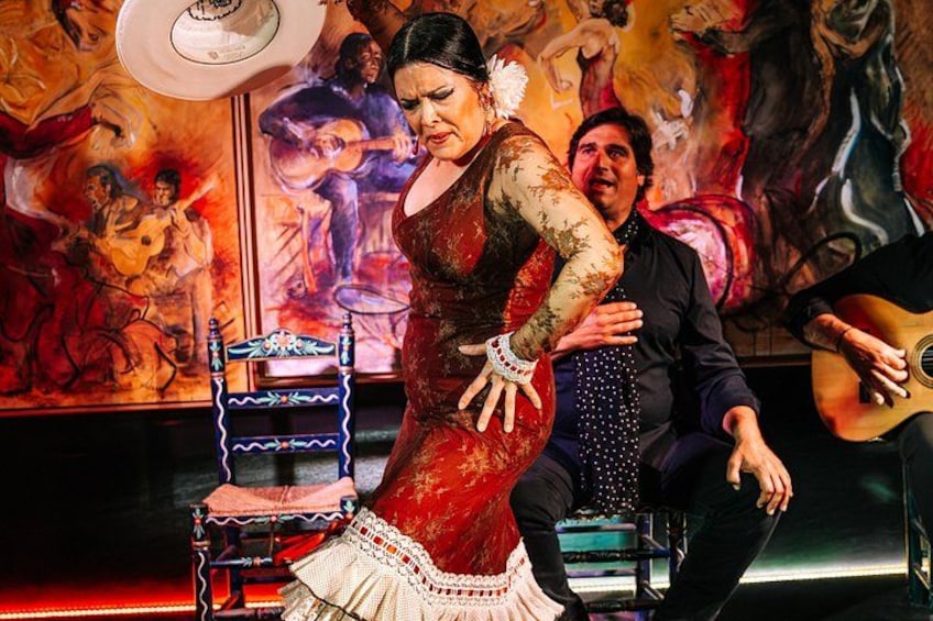 A woman in a red dress performing a dance, a man in a suit, and a guitar player in the background. 4