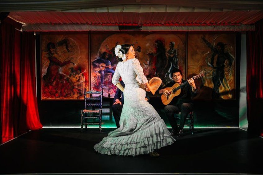 Una mujer con un vestido blanco en el escenario, con un guitarrista de fondo. 2