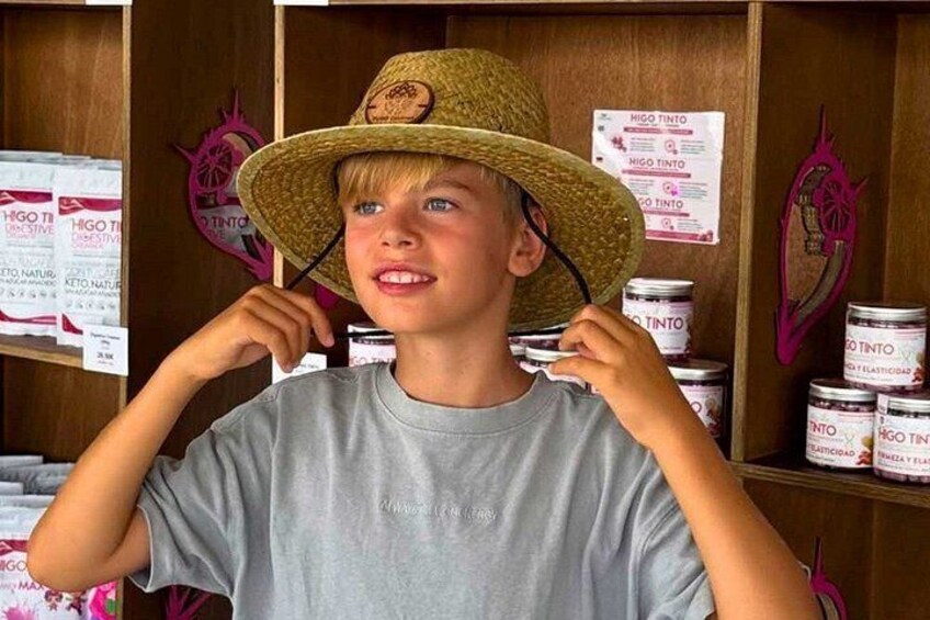A person wearing a straw hat and a grey t-shirt, standing in front of shelves with cans labeled 'HIGO TINTO'. 5