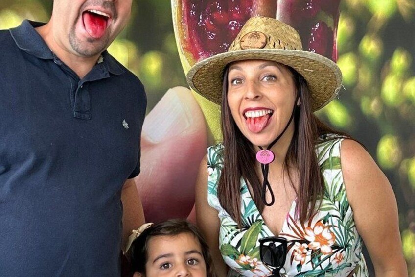 A person in a tropical print dress and straw hat, standing in front of a large fruit display. 4