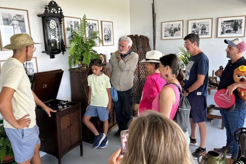 A group of people in a room with a vintage clock, framed pictures, and a potted plant. 2