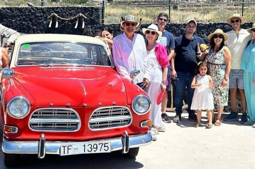 A vintage red car with the license plate TF-13975, parked in a sunny outdoor setting with a group of people standing behind it. 3