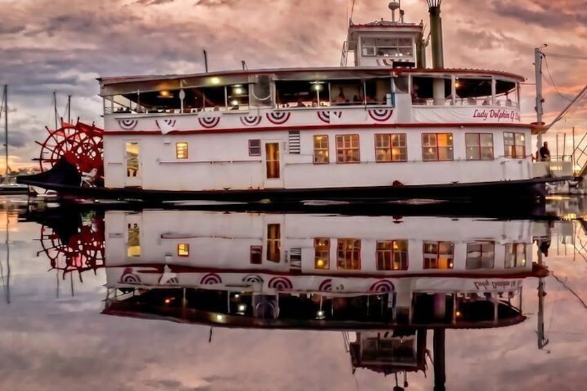 A steamboat with a large wheel and multiple decks, docked at a marina. 1