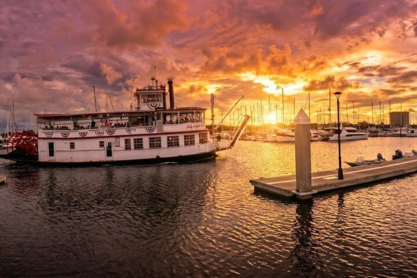 A riverboat docked at a pier with a sunset in the background. 3