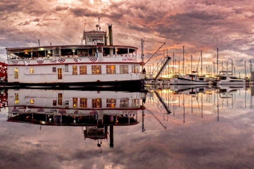 A riverboat docked at a marina with multiple boats, a cloudy sky, and a sunset reflection on the water. 4