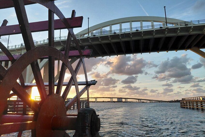 A bridge, a large water wheel, and a sunset over a body of water. 5