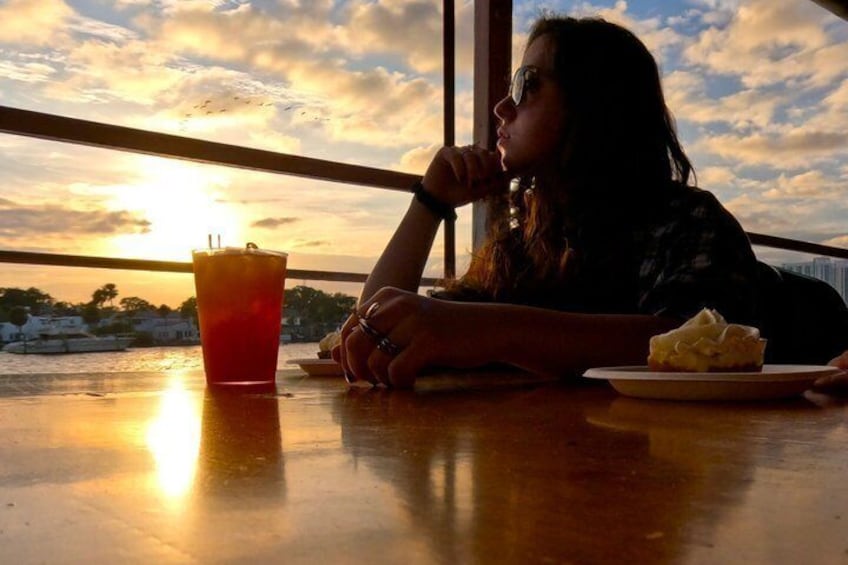 A person sitting at a table with a drink and a dessert, overlooking a sunset. 2