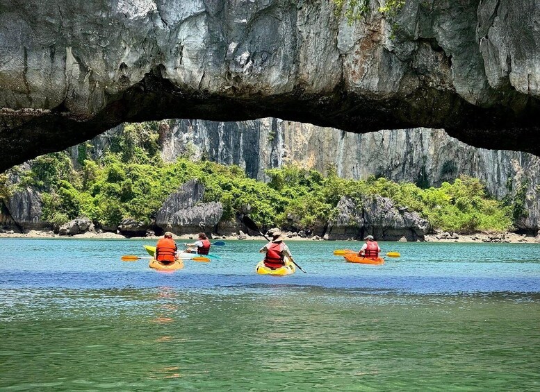Kayakers in orange life vests paddling under a large rock arch. 3