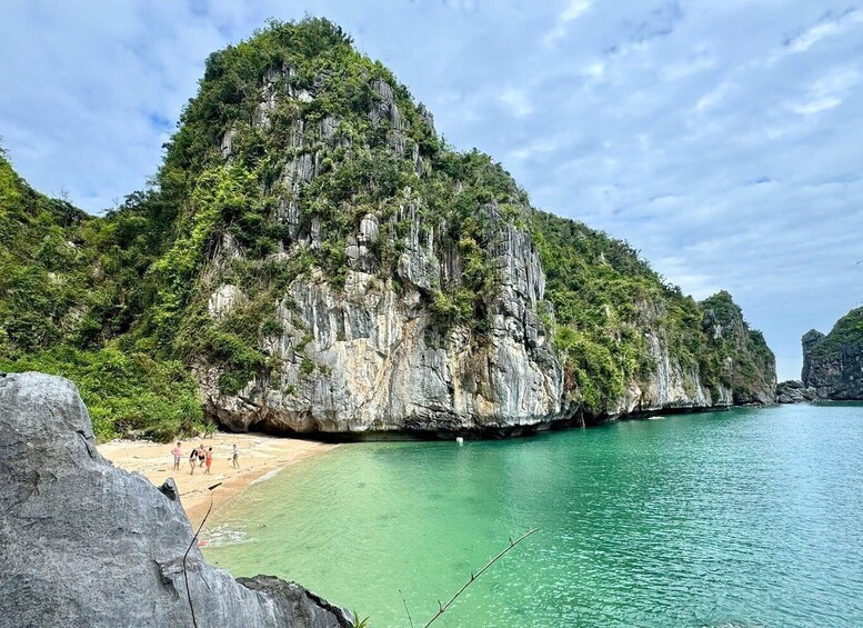 A coastal landscape with a large rock formation, clear turquoise water, and a sandy beach. 4