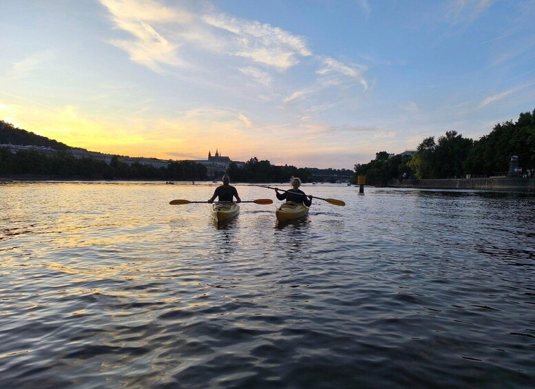 Two people kayaking on a river with a cityscape in the background during sunset. 3