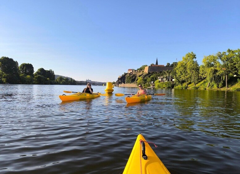 Two kayakers on a calm river with a bridge and buildings in the background. 1