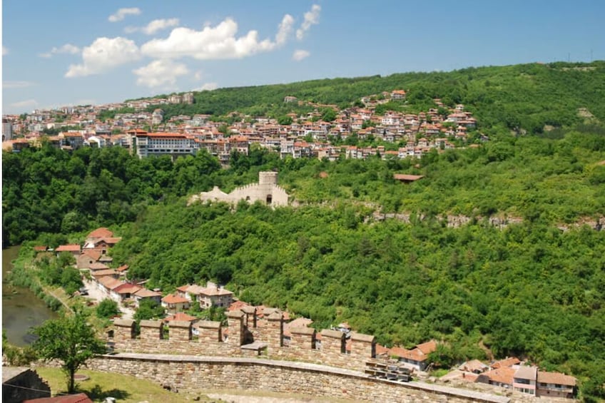 A hillside town with dense greenery, a stone wall, and a prominent tower. 3