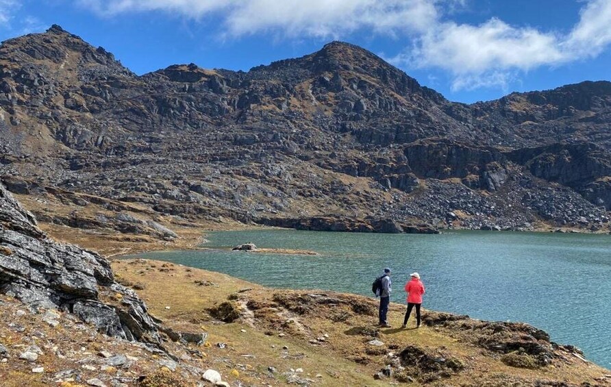 A mountainous landscape with a lake and two hikers. 2