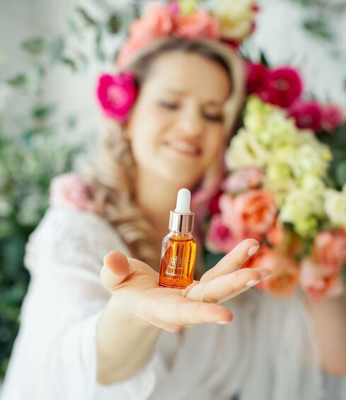 A person holding a small amber bottle with a white dropper cap, wearing a white garment and a floral headband. 1