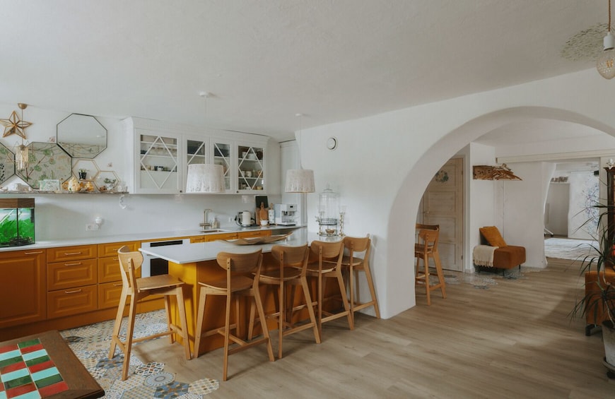 A modern kitchen with wooden cabinets, a dining table with chairs, and a cozy living area with a chair and a plant. 2