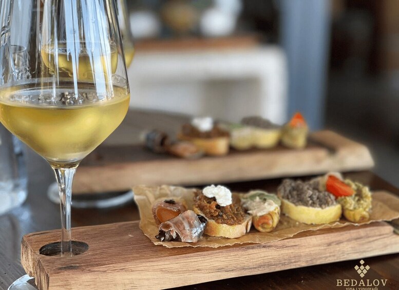 A glass of white wine and a wooden board with various appetizers. 2