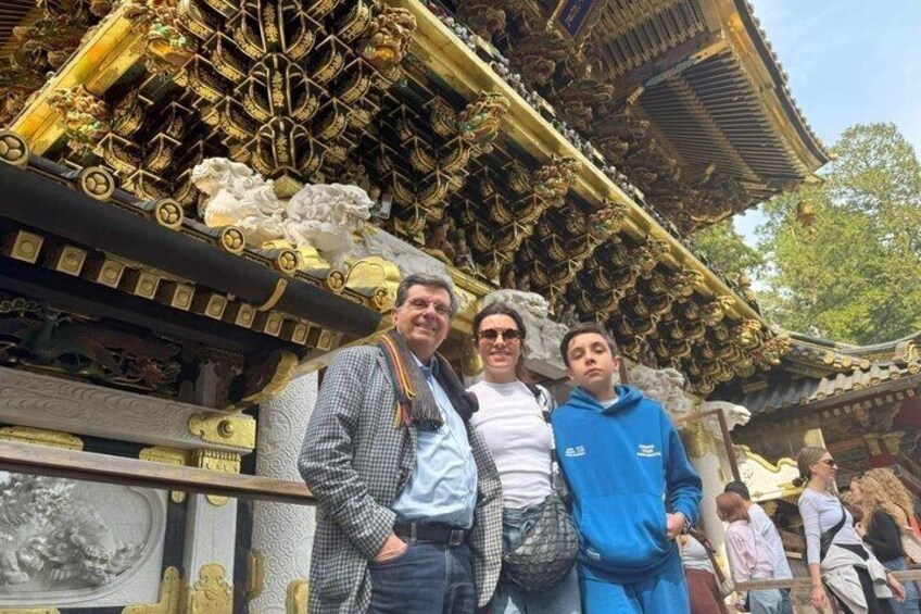 A group of people standing in front of a traditional ornate building with intricate golden details and a tiled roof. 1