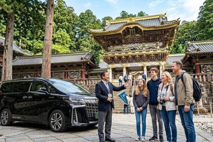 A traditional Japanese building with a golden roof, surrounded by trees and a black car parked nearby. 1