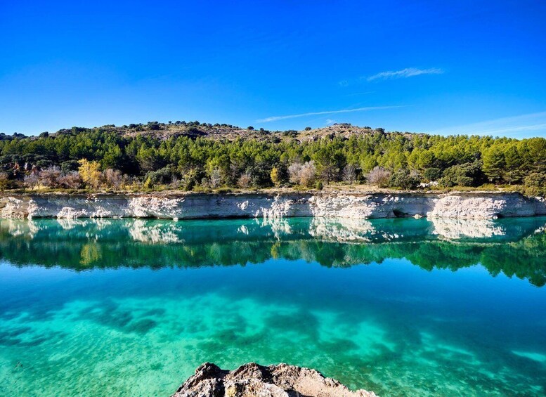 A clear turquoise lake with rocky shores and a forested hill in the background. 3