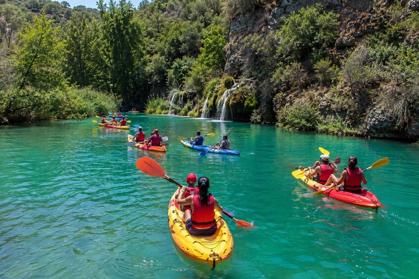 People kayaking on a clear river surrounded by lush greenery and a waterfall. 5
