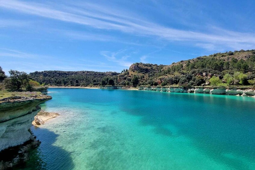 A coastal landscape with clear turquoise waters, rocky cliffs, and a forested hillside. 2