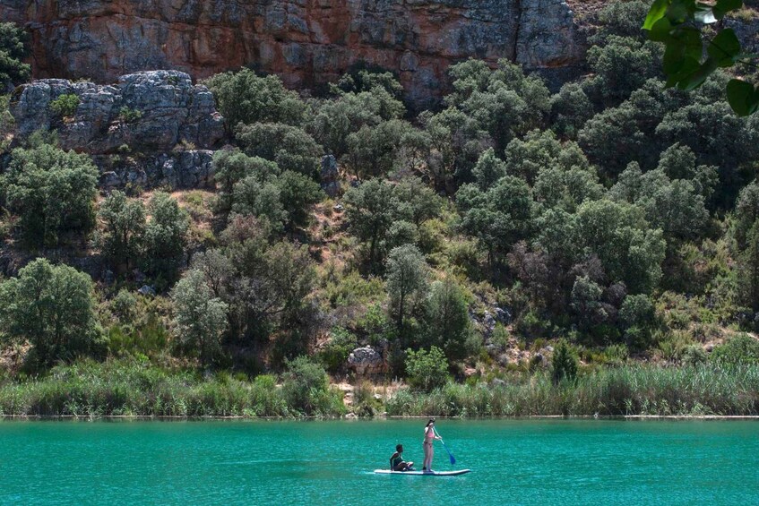Two people paddleboarding on a turquoise lake with a rocky cliff and dense greenery in the background. 4