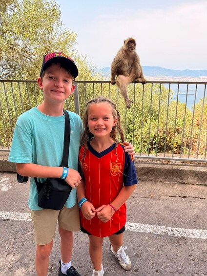 Two people standing in front of a railing with a monkey on a nearby railing. 2