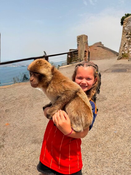 A person holding a monkey on a coastal path with stone structures and a body of water in the background. 4