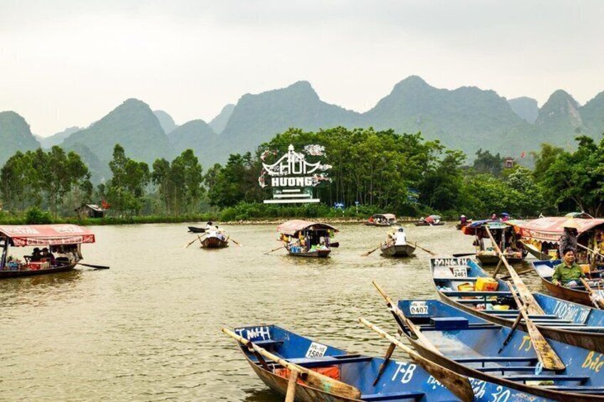 A river with boats, a sign for 'HUONG', and mountains in the background. 1