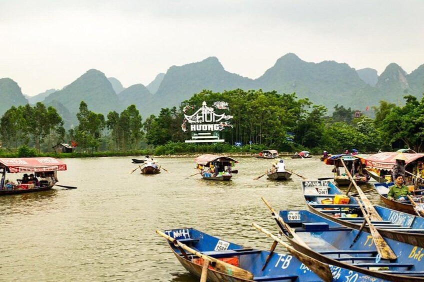 Un río con barcos, un cartel que dice 'HUONG' y montañas al fondo. 1