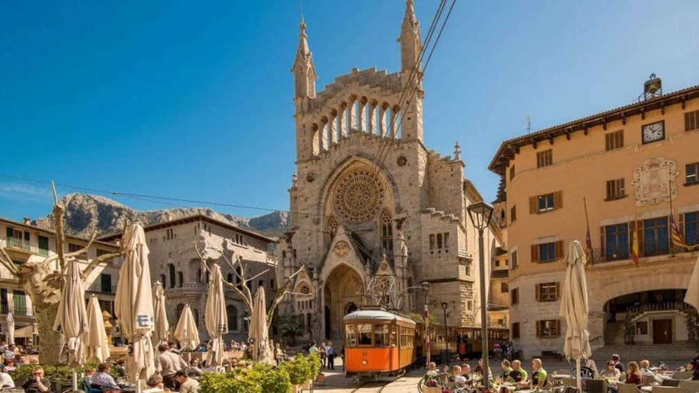 A historic cathedral with a prominent rose window, a tram in the foreground, and outdoor seating areas with umbrellas. 5