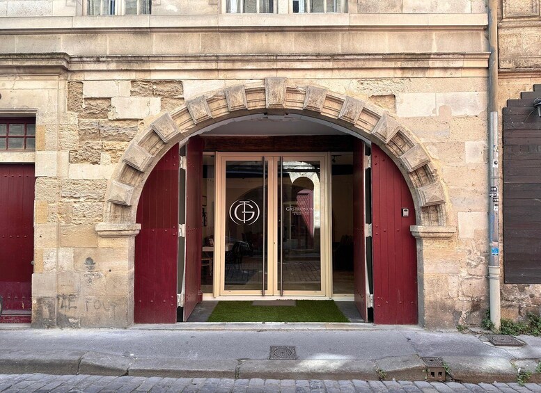 A building entrance with a red door, a glass door with a logo, and a stone archway. 2