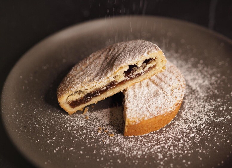 A half-eaten pastry dusted with powdered sugar on a dark plate. 1