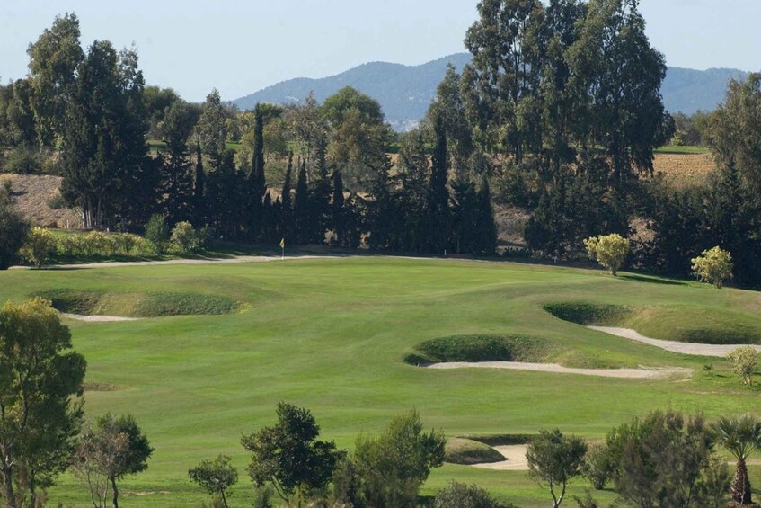 A golf course with sand bunkers, trees, and a mountainous backdrop. 4