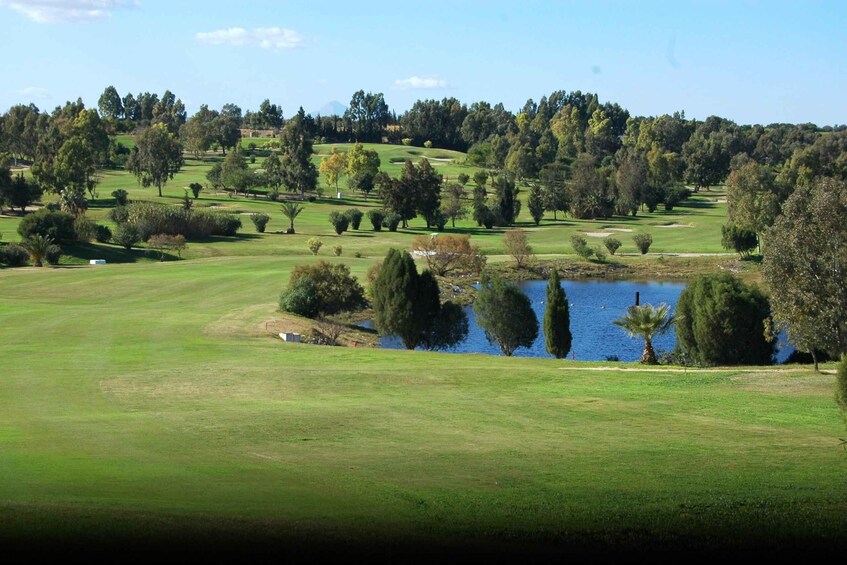 A golf course with a pond, trees, and rolling hills. 5