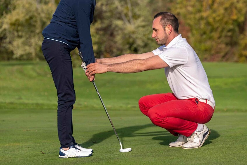 Two people on a golf course, one standing and one crouching, holding a golf club. 1