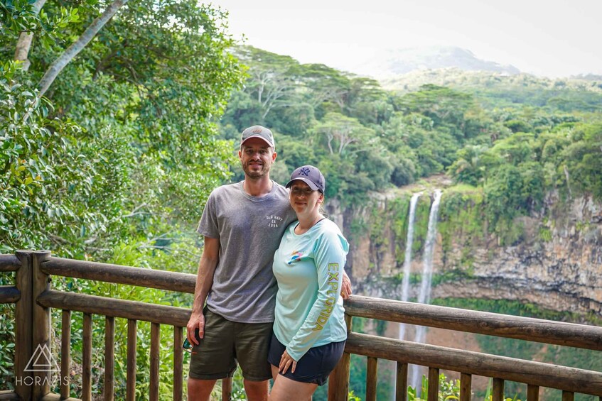 A couple standing on a wooden bridge with a waterfall in the background. 5