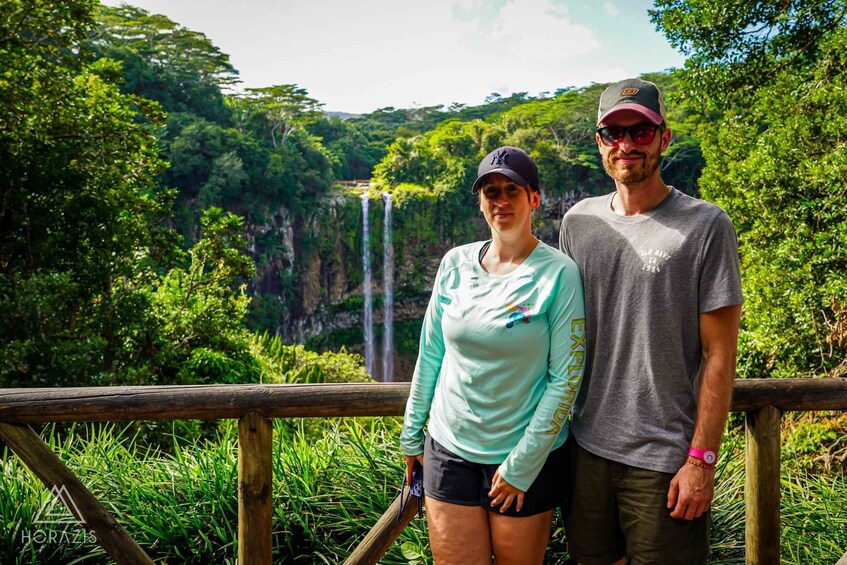 Two people standing by a wooden railing with a waterfall in the background. 2